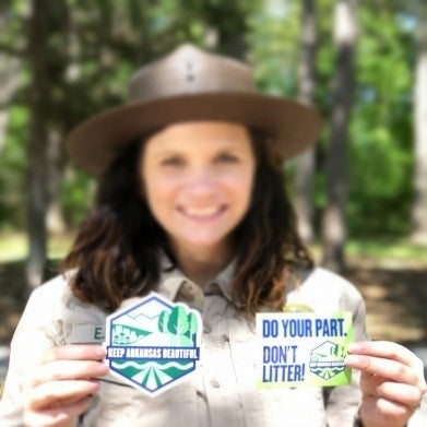 Park interpreter holding stickers with the Keep Arkansas logo and motto of Do Your Part, Don’t Litter